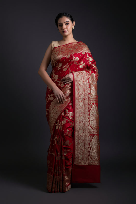 Woman wearing a red saree with gold patterns on a dark background